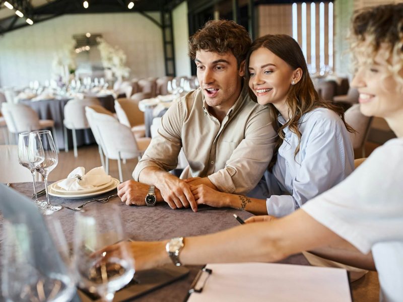 amazed-and-happy-couple-looking-at-laptop-near-event-organizer-at-festive-table-bridal-preparation.jpg